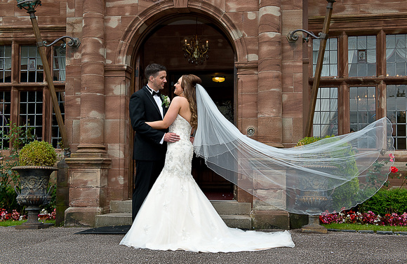 Bride-and-Groom-embrace-outside-Wrenbury-Hall-veil-extended-richard-linnett-photography